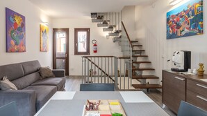 A modern living room with a sofa, a dining table, a staircase, and artwork on the walls. - Casa Vicolo San Giovanni Apartment with Private Terrace, Wi-Fi & Air Conditioning (Palermo)