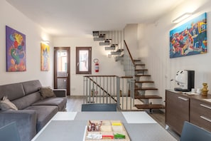 Un salon moderne avec un canapé, une table à manger, un escalier et des œuvres d’art accrochées aux murs.