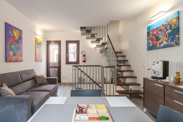 Un salon moderne avec un canapé, une table à manger, un escalier et des œuvres d’art accrochées aux murs.