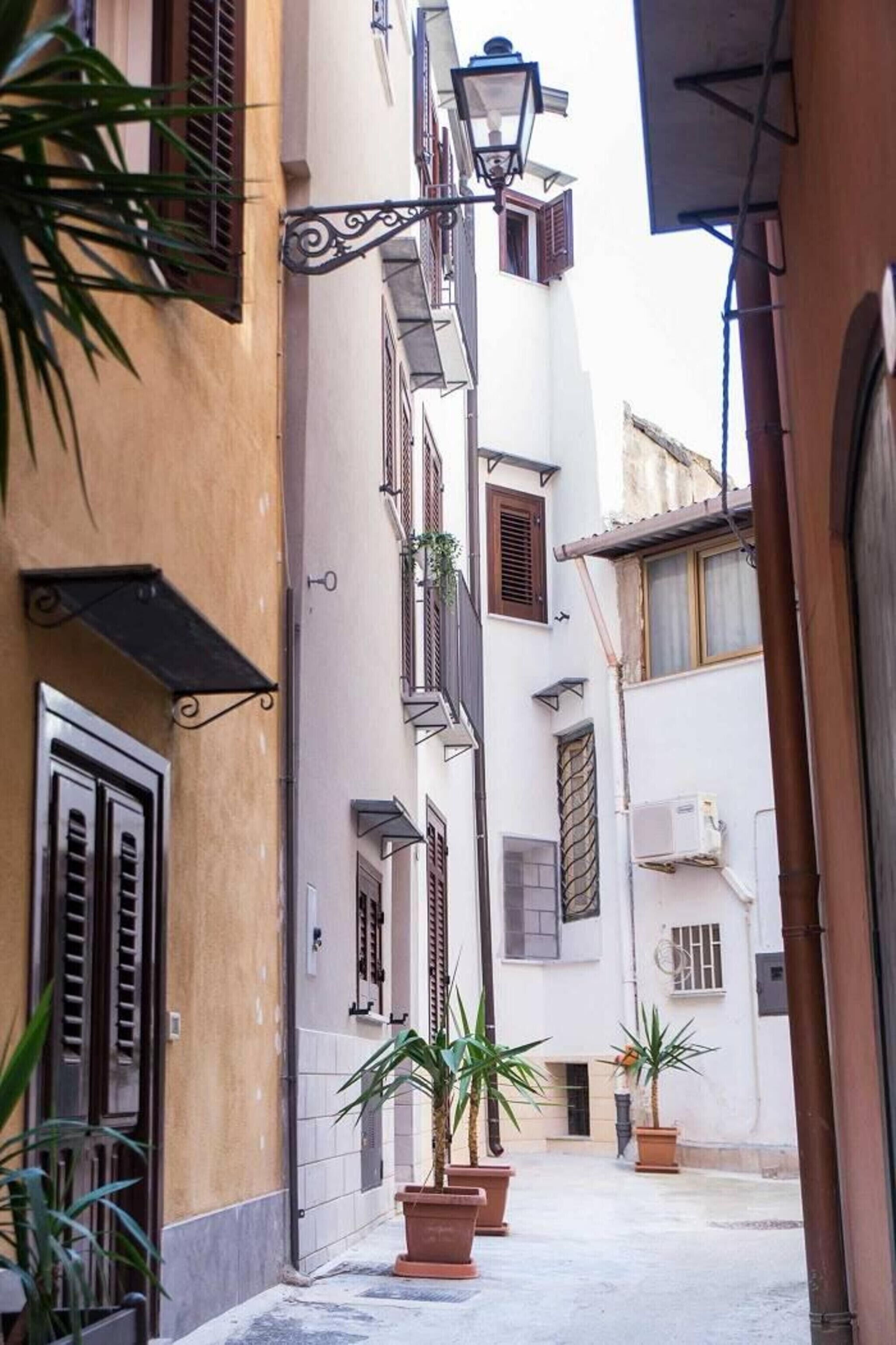 Una stretta via fiancheggiata da edifici, un lampione e vasi con piante.