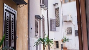A narrow street with buildings, a street lamp, and potted plants. - Casa Vicolo San Giovanni Apartment with Private Terrace, Wi-Fi & Air Conditioning (Palermo)