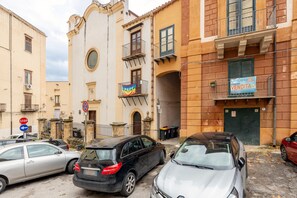 Une rue bordée de voitures garées, un immeuble avec une enseigne indiquant « UniCasa Vendita », et une banderole « PACE ».
