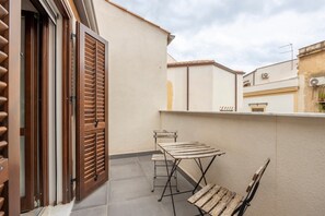 Un balcon avec une table et des chaises en bois, une porte coulissante et une vue sur les bâtiments voisins.