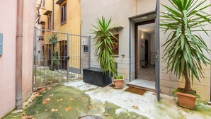 A courtyard with a metal gate, potted plants, a concrete floor, and a building entrance. - Casa Vicolo San Giovanni Apartment with Private Terrace, Wi-Fi & Air Conditioning (Palermo)