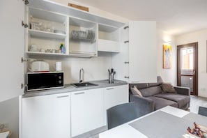 Une cuisine compacte avec des meubles blancs, un four à micro-ondes et un évier. Un coin repas est aménagé avec une table et des chaises.