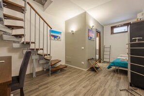 Une pièce avec un escalier en bois, un lit recouvert d’une couverture turquoise, un bureau et une chaise.