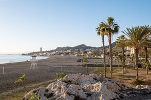 A beach with a lifeguard tower, palm trees, and a distant mountain.