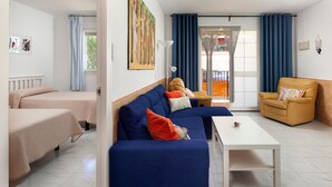 A room with a blue sofa, a yellow armchair, a white coffee table, and a bed with a beige cover. - Apartment 'Casa Santo Front Beach' with Private Terrace and Wi-Fi (Cala del Moral)