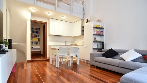 A modern living room with a grey sofa, a dining area with white chairs, and a kitchen with white cabinets. - Cozy flat in Isola facing Bosco Verticale - Intrho (Milan)
