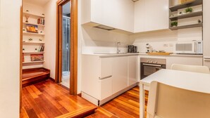 A compact kitchen with white cabinets, a microwave, and a sink. There is a wooden staircase leading to another room. - Cozy flat in Isola facing Bosco Verticale - Intrho (Milan)