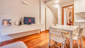 A modern living room with a white brick wall, a flat-screen TV, a dining table with white chairs, and a wooden floor. - Cozy flat in Isola facing Bosco Verticale - Intrho (Milan)