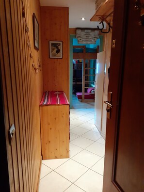 A narrow hallway with wooden walls, a bench, and a door leading to a room with a bunk bed.