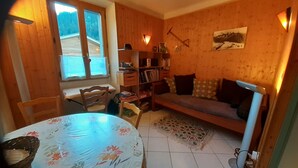 Habitació acollidora amb paret de fusta, un sofà, una biblioteca, una taula de dinar i una finestra.