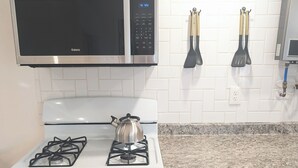 A kitchen with a gas stove, a microwave, and a stainless steel range hood. There are two spatulas hanging on the wall. - Charming Cottage in Central Salem (Salem)
