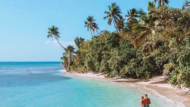 A beach with clear turquoise water, palm trees, and a couple in the water. - 3-bedroom in superb cozy Arecibo River with WiFi, AC (Puerto Rico)