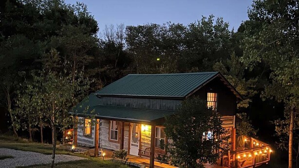 Een rustieke chalet met een groen metalen dak, houten gevel en een veranda met lichtjes.