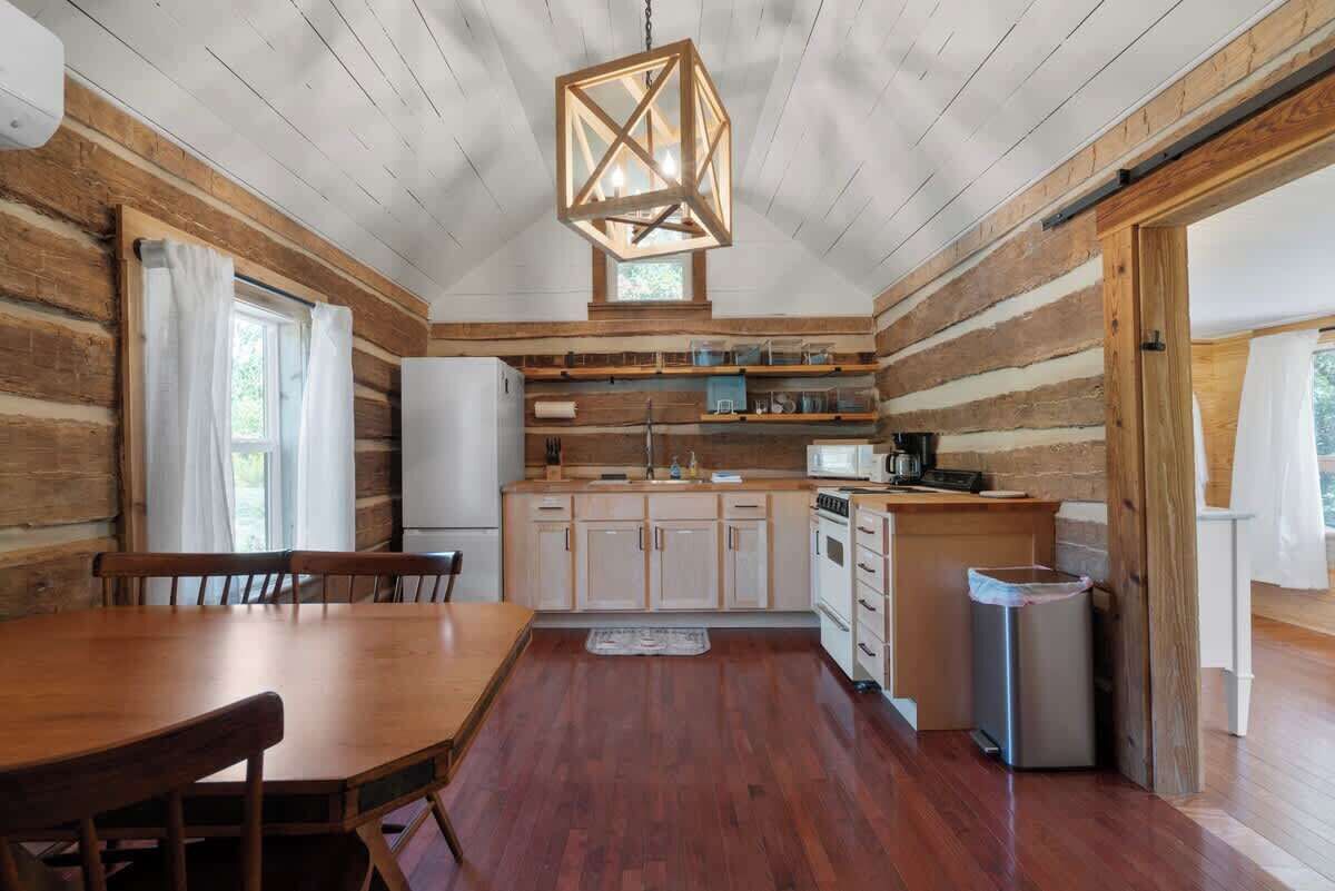 Una cucina in stile baita con pareti in legno, un tavolo da pranzo, sedie, una lampada a sospensione e un piccolo cestino.