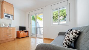 Ein modernes Wohnzimmer mit grauem Sofa, Holzschränken, einem Flachbildfernseher und einer Glasschiebetür, die auf einen Balkon im Freien führt.