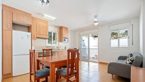 Eine moderne Küche mit Holzausstattung, einem Esstisch mit Stühlen, einem grauen Sofa und einer Schiebetür zum Balkon.