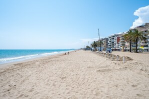 A beach with a sandy shore, a clear blue sky, and buildings in the background. - Apartment 'Dorada 1-2' with Shared Pool, Shared Garden and Wi-Fi (Calafell)