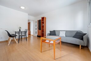 A modern living room with a glass-top coffee table, a grey sofa, and a dining area with a small table and chairs. - Apartment 'Dorada 2-2' with Shared Pool, Shared Garden and Wi-Fi (Calafell)