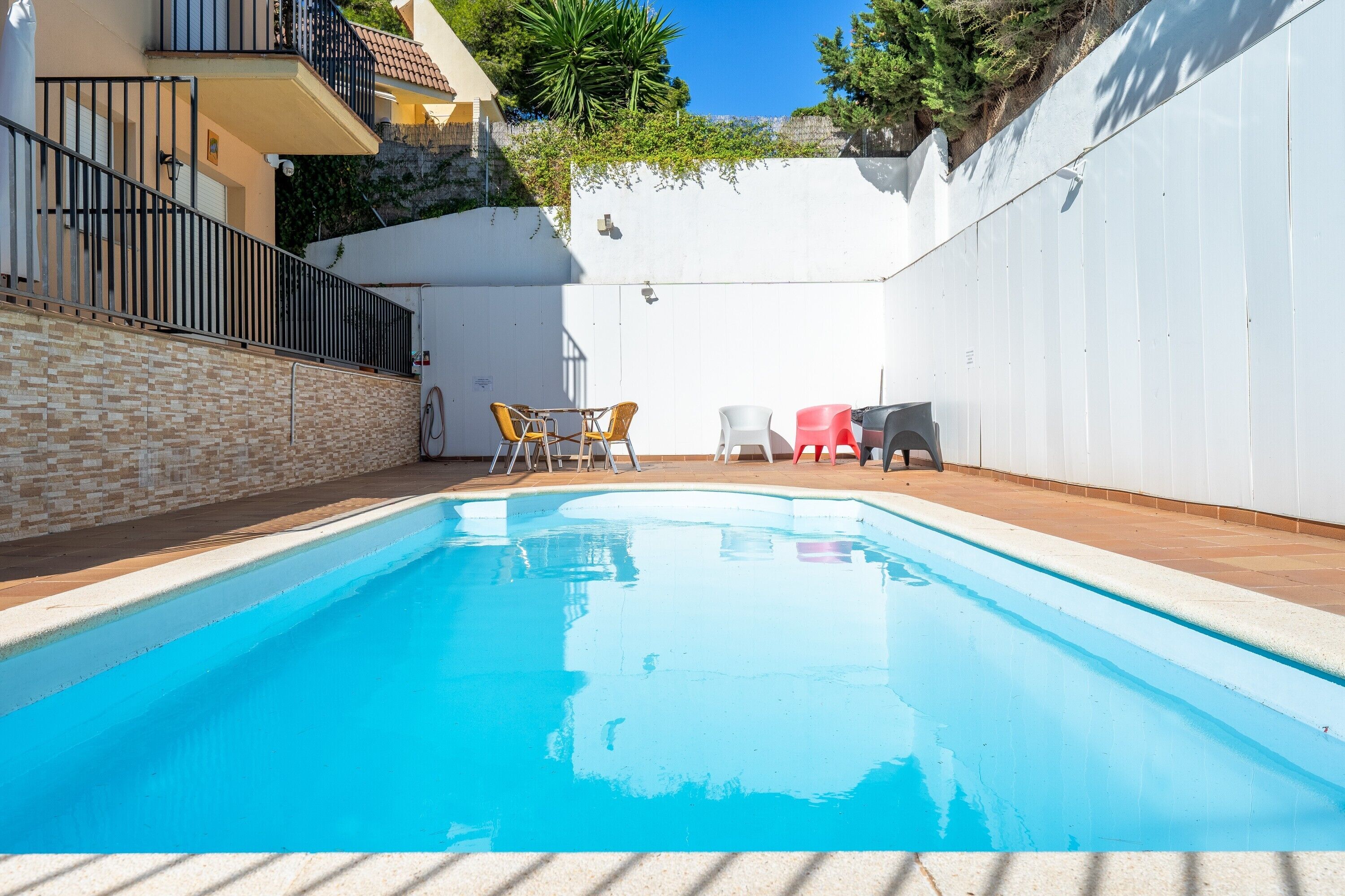 A swimming pool with a tiled deck, a white wall, and a brick wall with a metal railing.