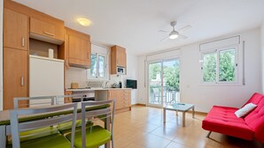 A modern kitchen with wooden cabinets, a dining area with green chairs, a red sofa, and a balcony with a view. - Apartment 'Dorada 2-3' with Shared Pool, Private Terrace and Wi-Fi (Calafell)