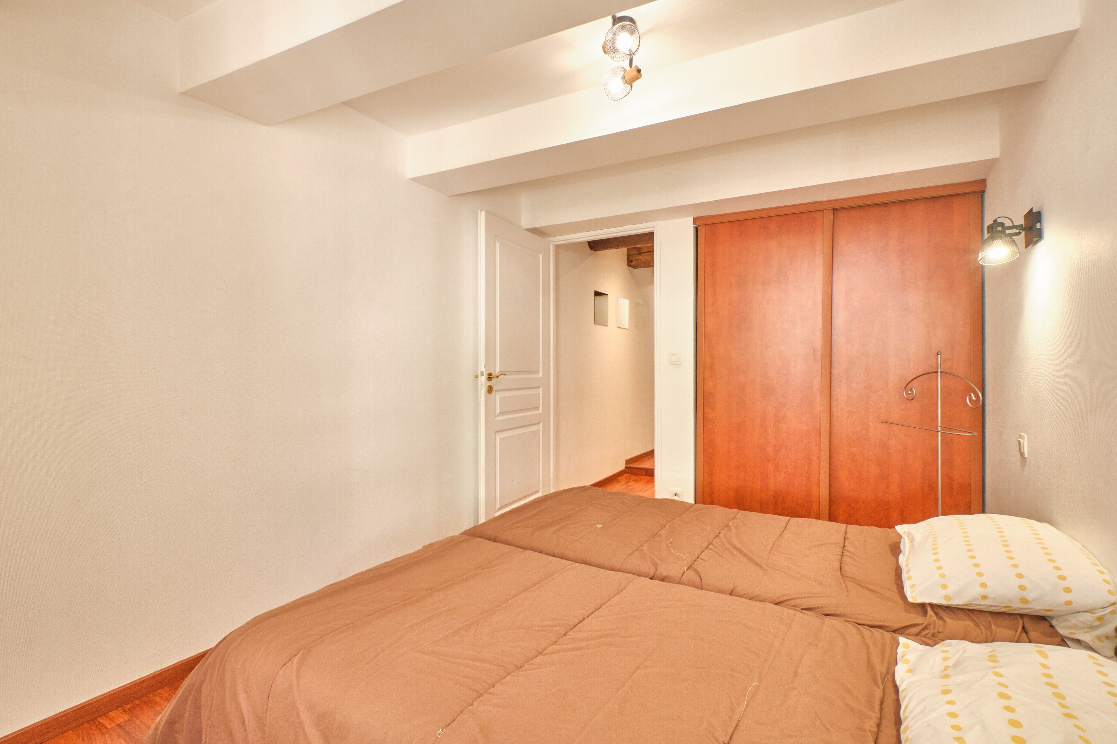 A bedroom with a large bed, a wooden wardrobe, and a wall-mounted light fixture.