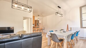 Uma sala de jantar moderna com uma mesa comprida, cadeiras e uma televisão ao fundo.