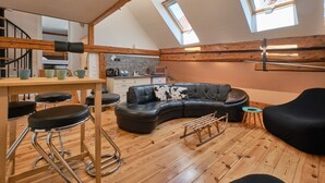 Quarto estilo loft com piso de madeira, sofá de couro preto, mesa de jantar com bancos e um skylight.