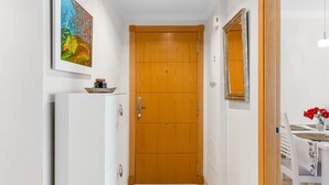 A narrow hallway with a wooden door, a white refrigerator, a painting, and a table with red flowers. - Benalmádena-Arenal Golf Apartment with Shared Pool, Wi-Fi, and Air Conditioning (Benalmádena)