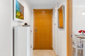 A narrow hallway with a wooden door, a white refrigerator, a painting, and a table with red flowers.