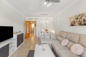 A modern living room with a flat-screen TV, a sofa, a coffee table, and a dining area in the background.