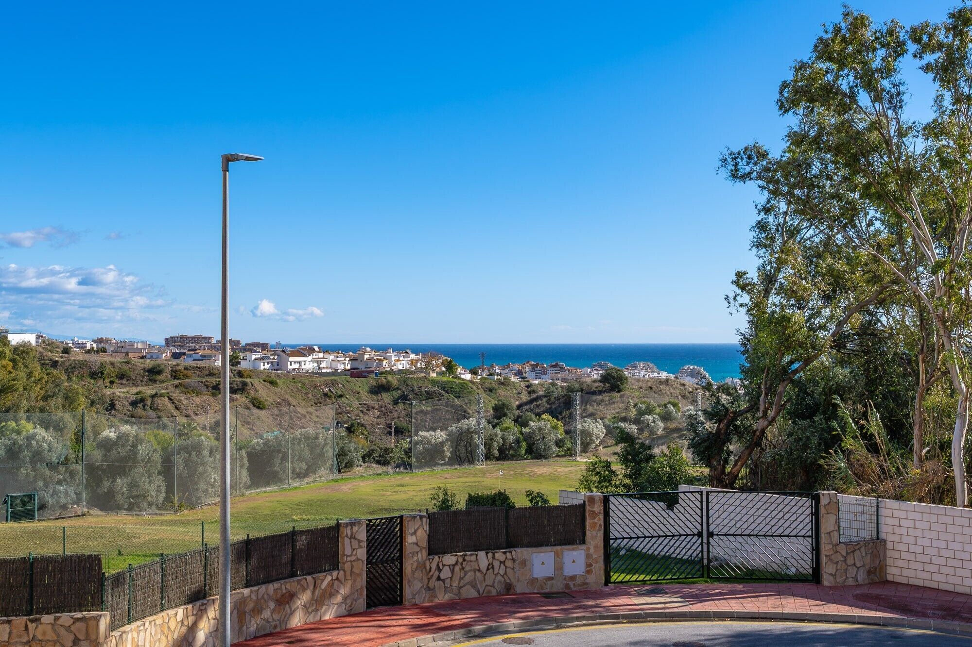 A coastal view with a paved area, a metal gate, and a street lamp.