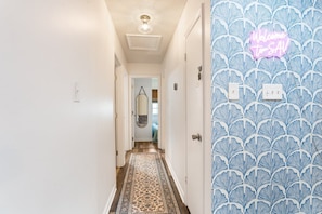 A hallway with patterned wallpaper, a neon sign, and a patterned rug.