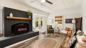 Un salon avec une cheminée, un logo Netflix, un ventilateur de plafond et un canapé.