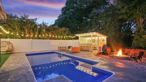 En baghave med swimmingpool, udendørs møbler og bålsted.