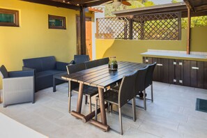 A patio with a wooden table, wicker chairs, a sofa, and a bar area.