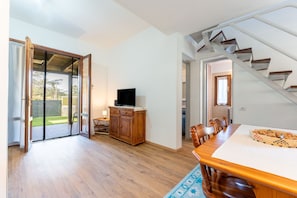 Une pièce spacieuse avec une table à manger en bois, un téléviseur posé sur un meuble et un escalier menant à un autre niveau.