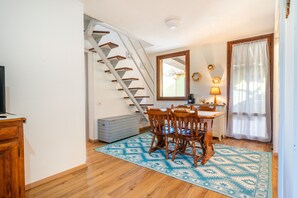A dining area with a wooden table and chairs, a staircase, a window with curtains, and a television on a cabinet.