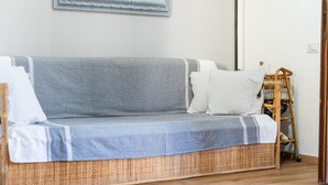 Un sofá gris con almohadones a rayas, una silla de mimbre y una escalera de madera frente a una pared blanca.
