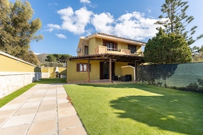 Une maison à deux étages dotée d’un patio couvert, d’une pelouse bien entretenue et d’un mur en pierre.