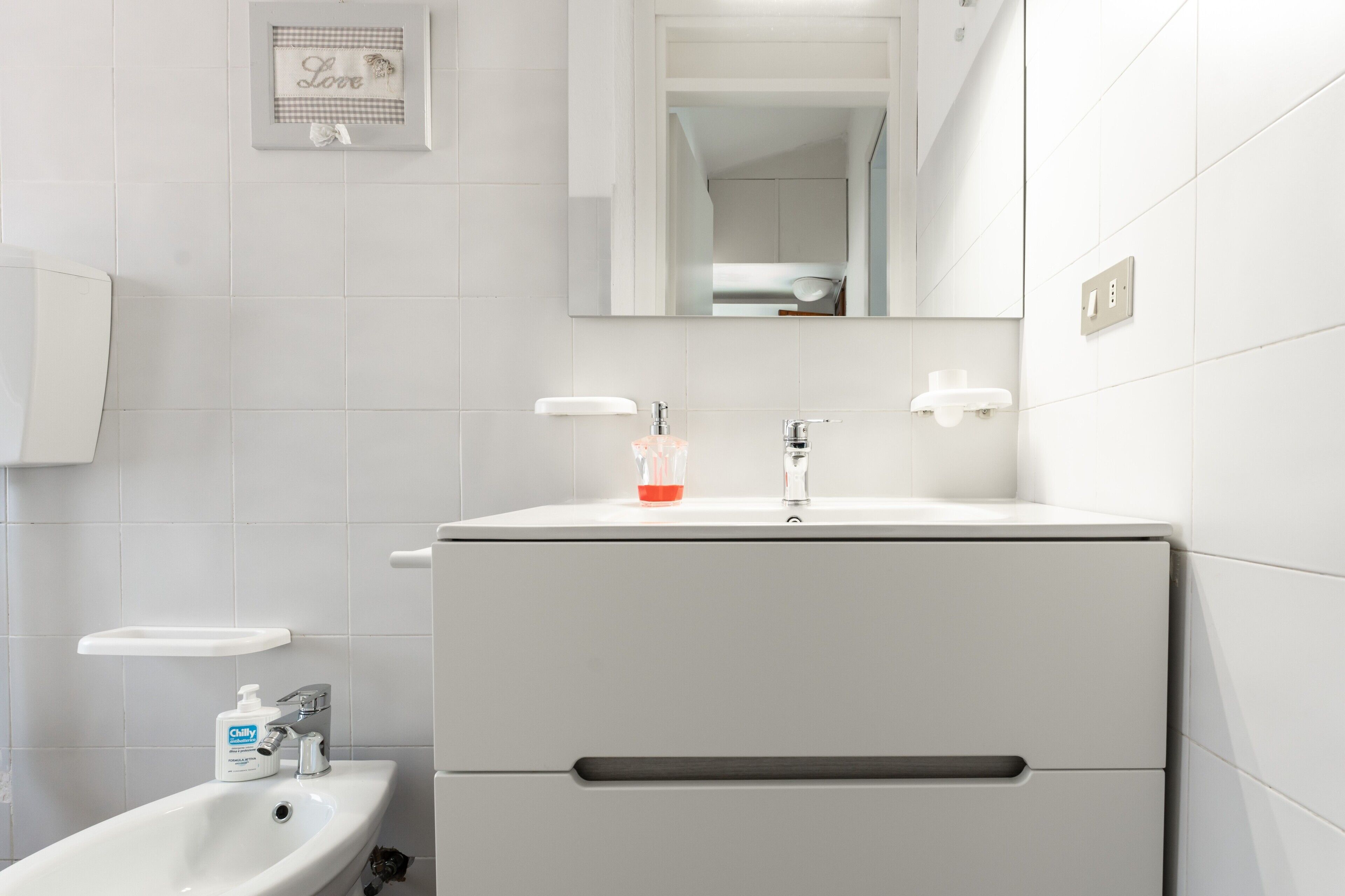 A bathroom with a white sink, mirror, and a framed picture on the wall.