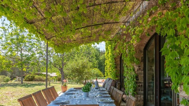 An outdoor dining area with a long table set for a meal, surrounded by chairs, and covered by a pergola with climbing plants. - Rural House 'Mas Darovie' with Mountain View, Wi-Fi and Air Conditioning (Foixá)