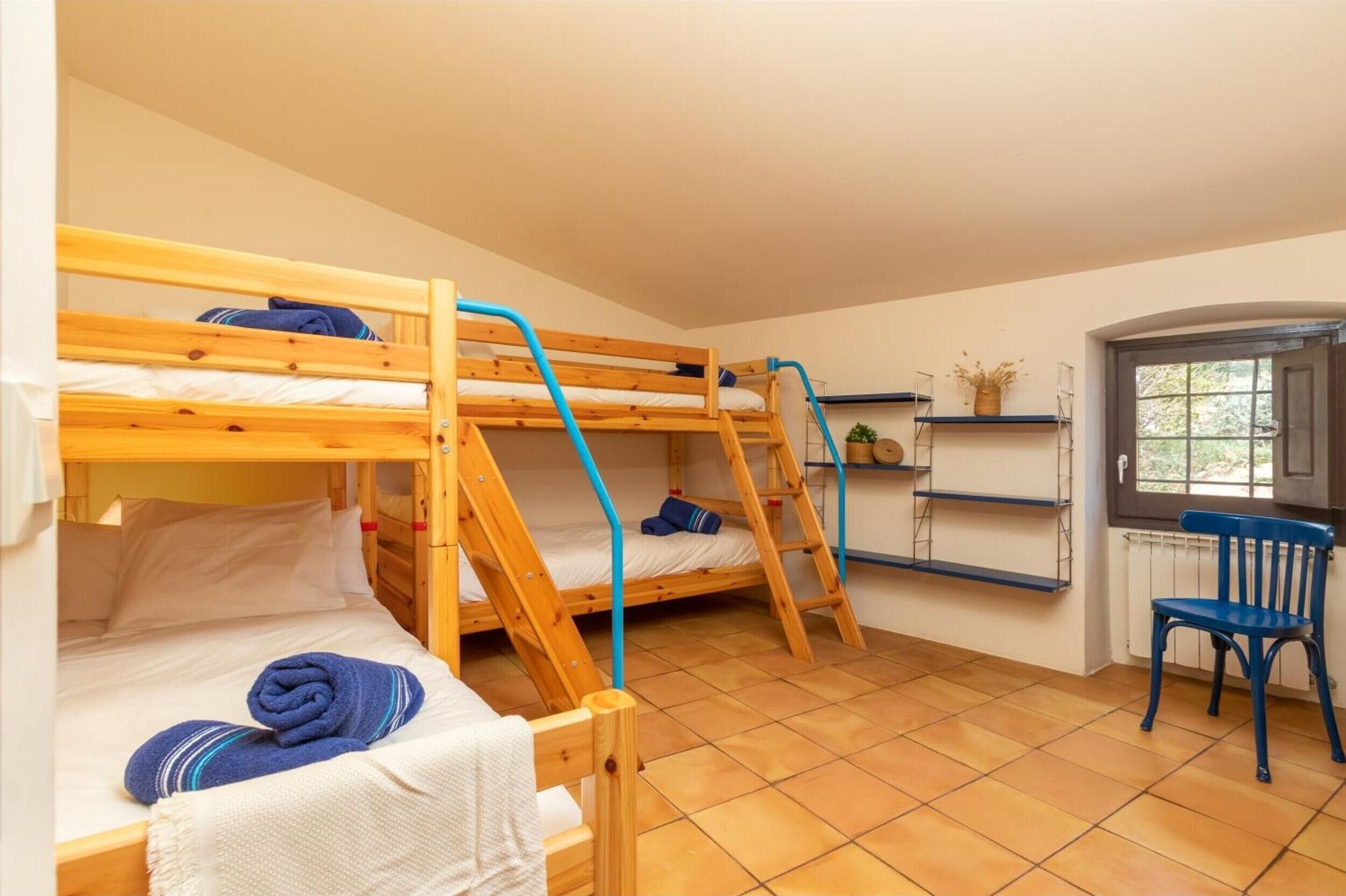 A dormitory room with bunk beds, a chair, a radiator, and a window.