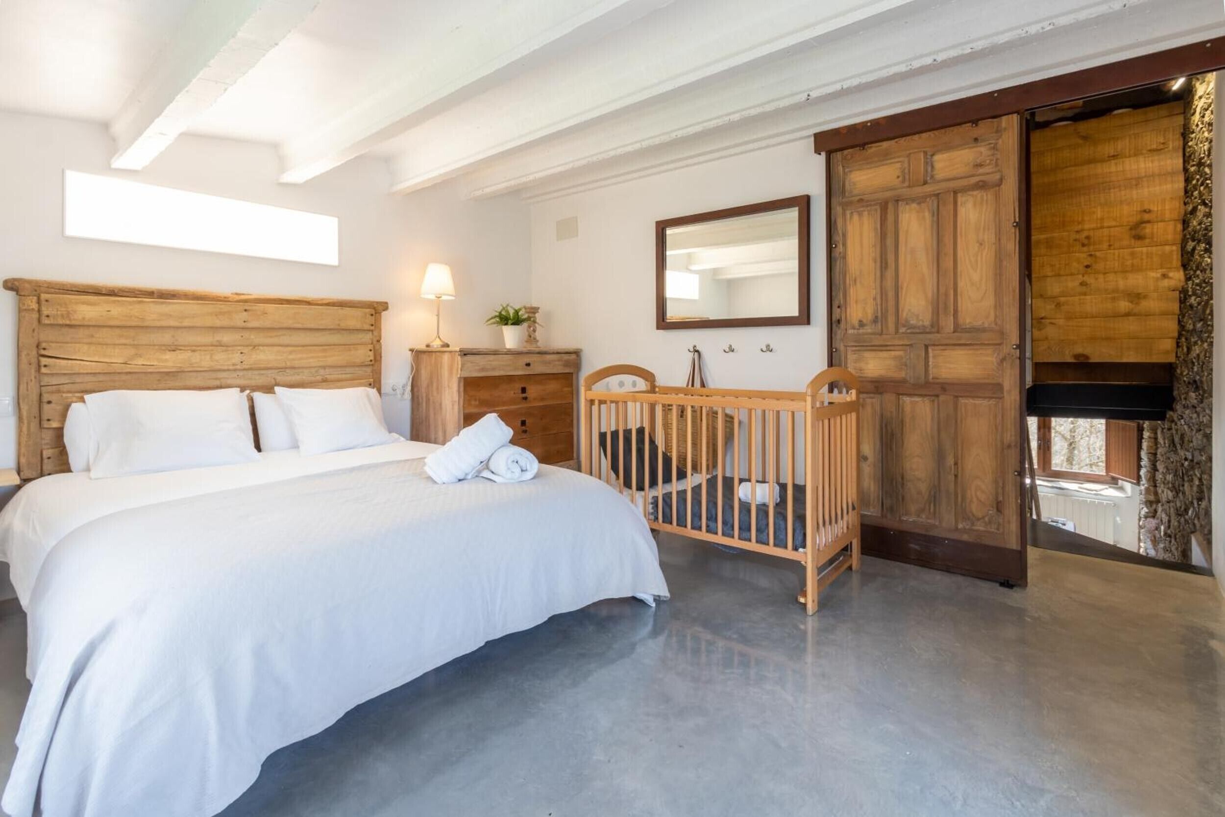 Ein Schlafzimmer mit einem hölzernen Bett, einem Kinderbett, einer Kommode, einem Spiegel und einer großen Holztür.
