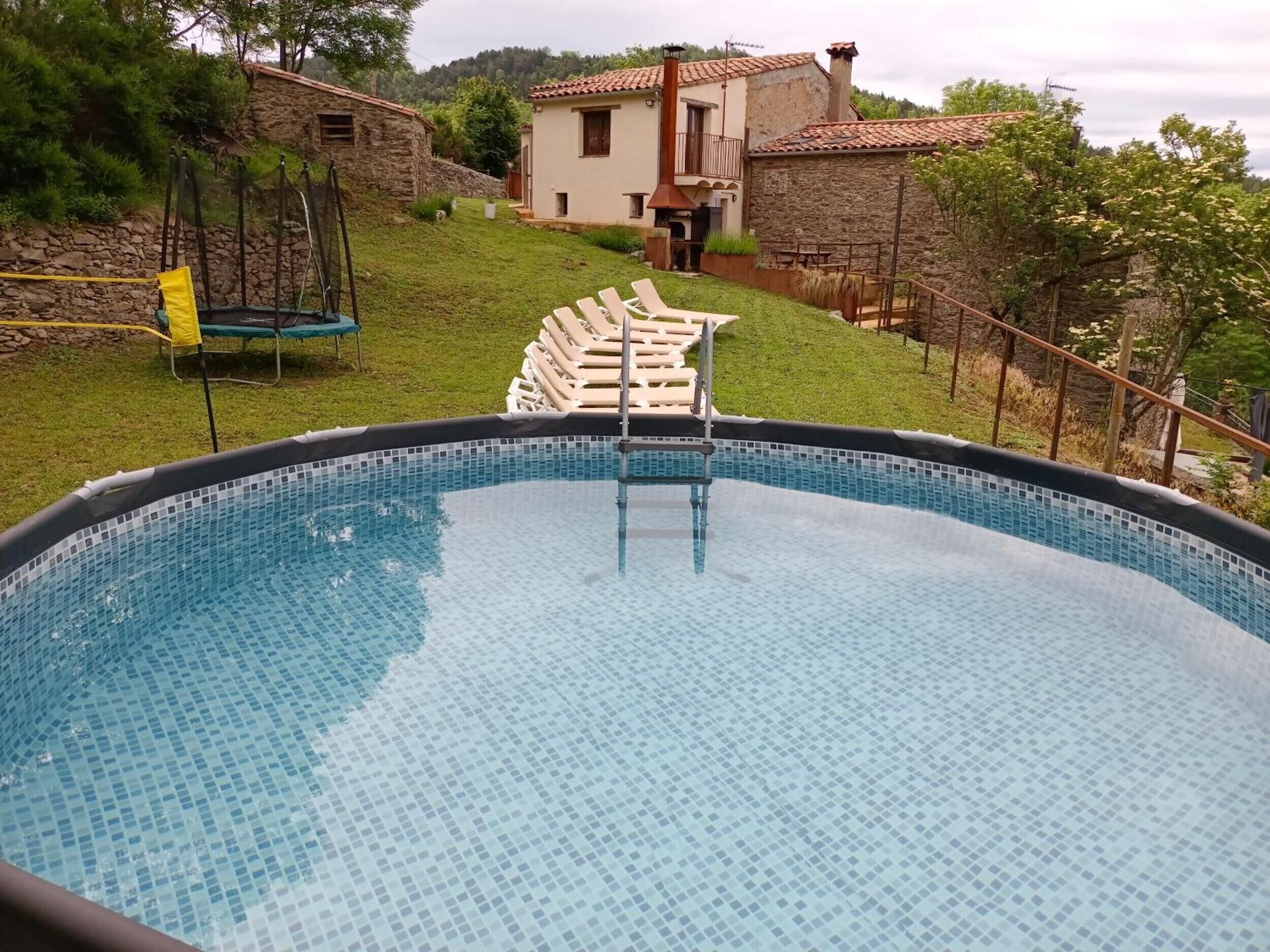 A swimming pool with a tiled edge, surrounded by a grassy area and a stone wall.