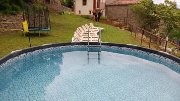 A swimming pool with a tiled edge, surrounded by a grassy area and a stone wall.