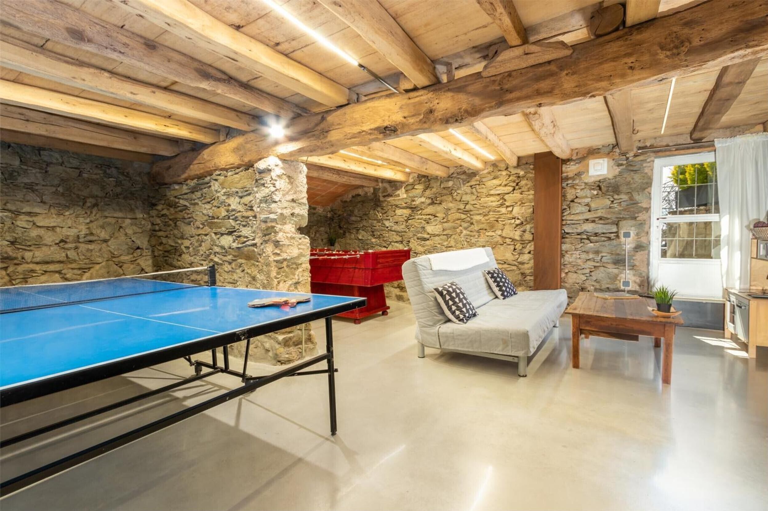 Una habitación con mesa de ping pong, un sofá, una mesa de centro de madera y paredes de piedra.