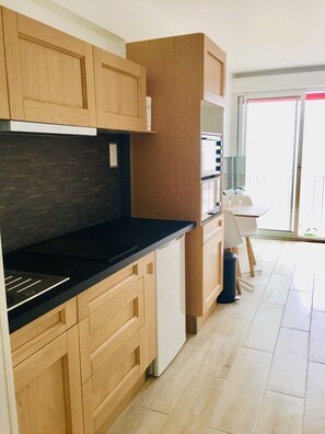 A modern kitchen with wooden cabinets, a black countertop, and a built-in oven. - Studio 'Wonderful Studio Facing the Sea' (Royan)